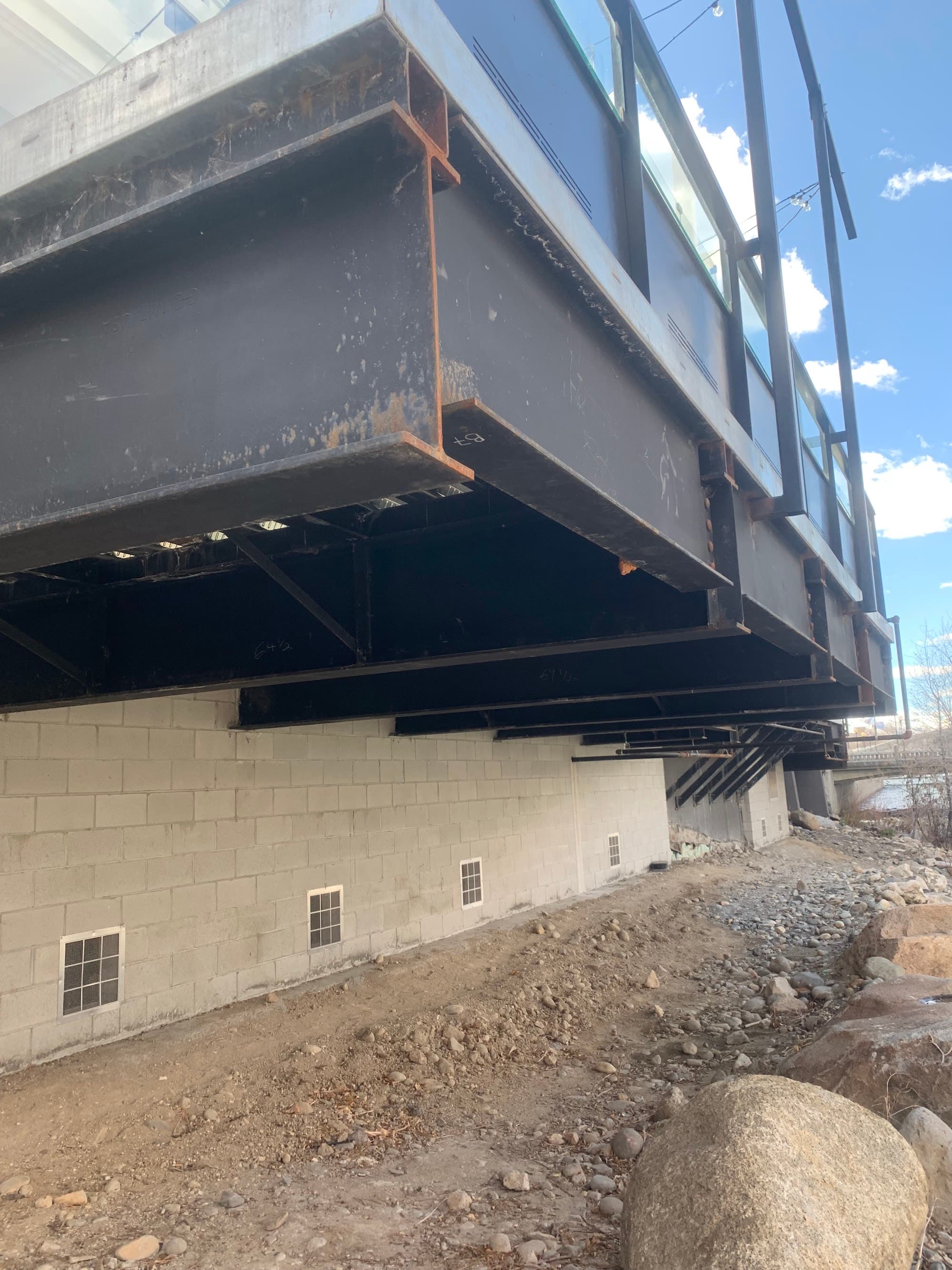 Heavy steel beam structure cantilevered over CMU block wall with glass railing — structural engineering detail